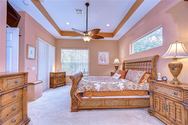 carpeted bedroom with multiple windows, a raised ceiling, and ceiling fan