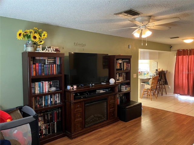 living room with ceiling fan, light hardwood / wood-style flooring, and a textured ceiling