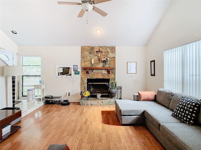 living room with ceiling fan, high vaulted ceiling, a stone fireplace, and light hardwood / wood-style floors