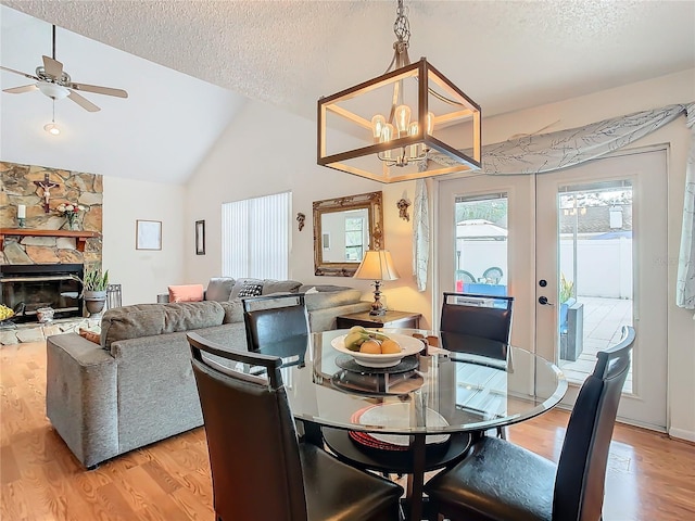 dining area featuring lofted ceiling, a textured ceiling, light hardwood / wood-style floors, and a stone fireplace