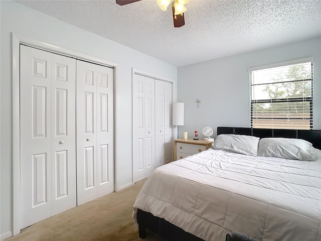 carpeted bedroom with ceiling fan, two closets, and a textured ceiling