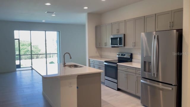 kitchen featuring stainless steel appliances, a kitchen island with sink, sink, and gray cabinetry