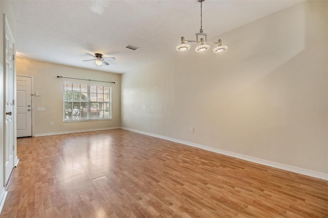 empty room with ceiling fan with notable chandelier, light hardwood / wood-style flooring, and a textured ceiling