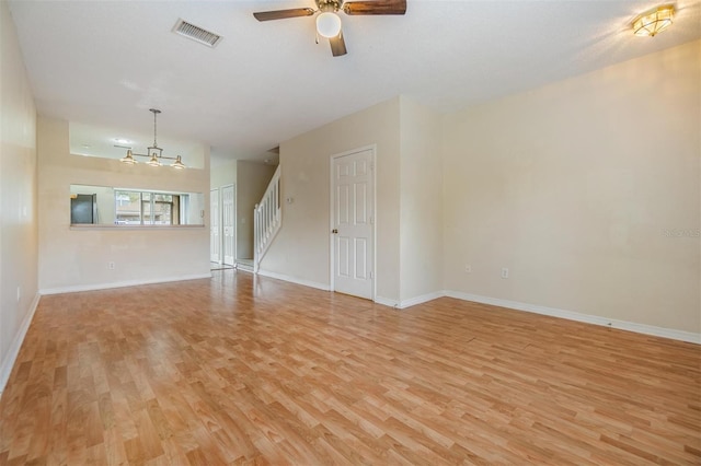 unfurnished living room with ceiling fan with notable chandelier and light hardwood / wood-style flooring