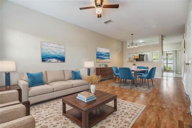 living room with ceiling fan with notable chandelier and light hardwood / wood-style floors