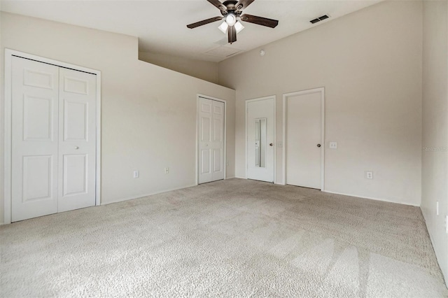 unfurnished bedroom featuring ceiling fan, multiple closets, and carpet flooring