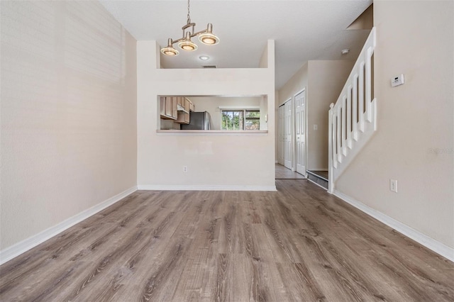 unfurnished living room with visible vents, baseboards, wood finished floors, and stairs