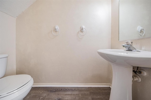 half bathroom with lofted ceiling, wood finished floors, toilet, and baseboards