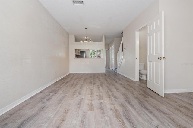 spare room featuring a chandelier, light wood-style floors, visible vents, and baseboards