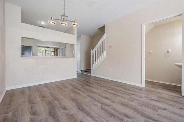 unfurnished living room with wood finished floors, visible vents, baseboards, and stairway