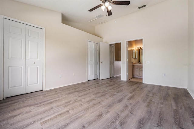 unfurnished bedroom featuring wood finished floors, ensuite bathroom, attic access, multiple closets, and lofted ceiling