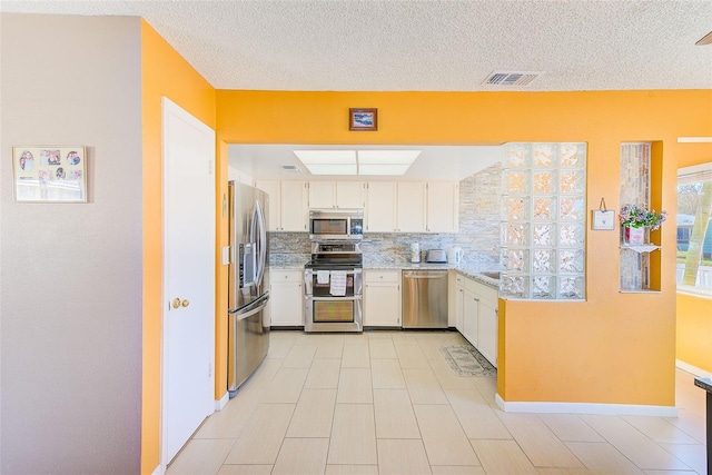 kitchen featuring stainless steel appliances, white cabinetry, backsplash, and a textured ceiling