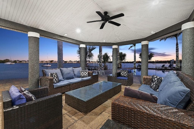 patio terrace at dusk with an outdoor hangout area, ceiling fan, and a water view