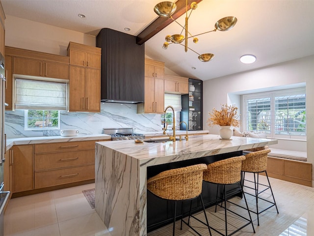 kitchen with a healthy amount of sunlight, a kitchen island with sink, vaulted ceiling with beams, and a kitchen bar