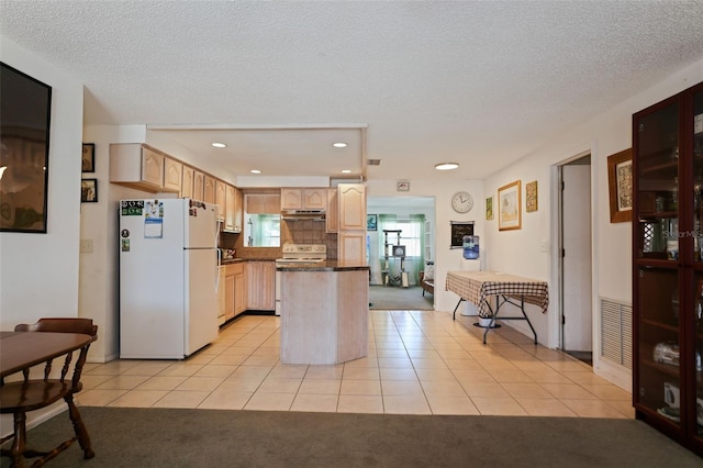 kitchen with light brown cabinetry, white appliances, a textured ceiling, and light tile patterned flooring