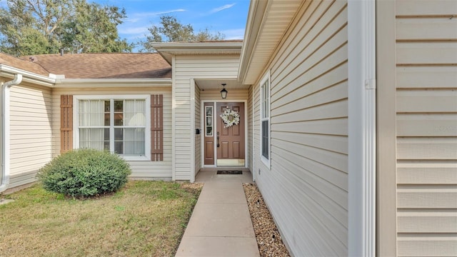 doorway to property featuring roof with shingles and a lawn
