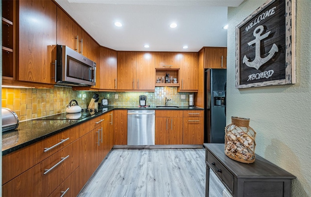 kitchen with sink, light hardwood / wood-style flooring, dark stone countertops, decorative backsplash, and black appliances