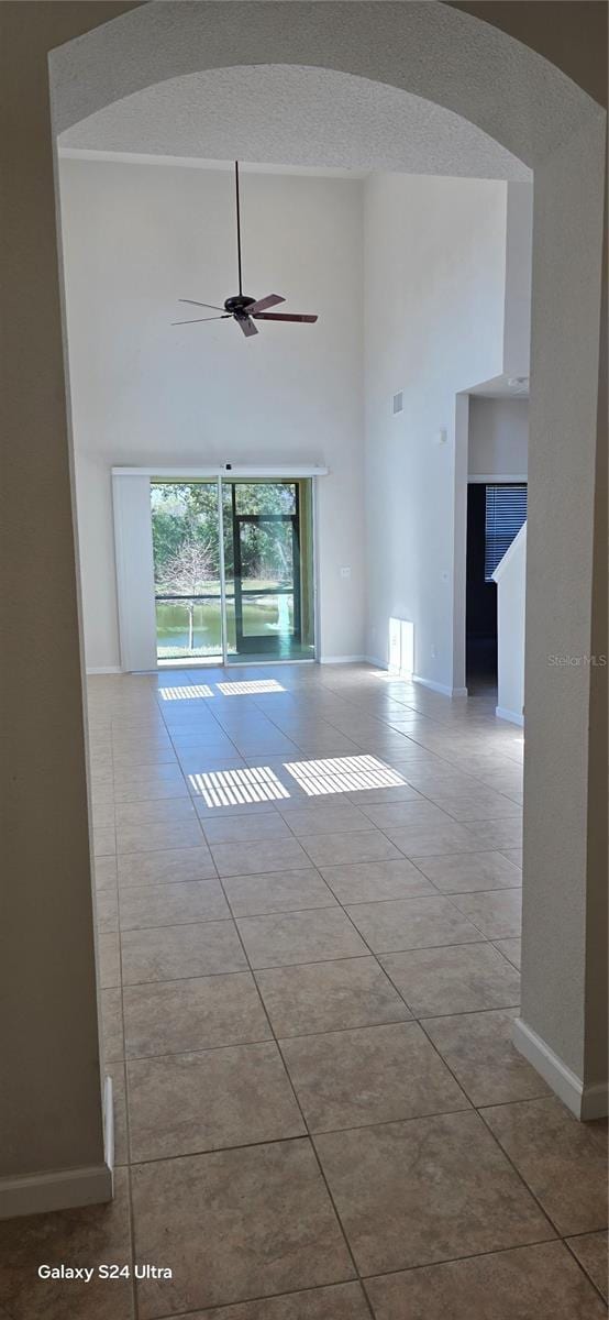 spare room featuring light tile patterned floors, a towering ceiling, a textured ceiling, and ceiling fan