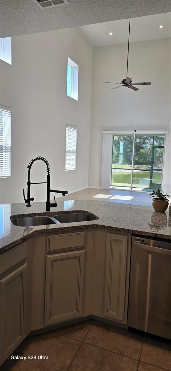 kitchen featuring light stone countertops, a towering ceiling, stainless steel dishwasher, and sink