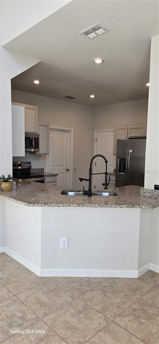 kitchen featuring sink, white cabinetry, stainless steel appliances, light stone countertops, and kitchen peninsula