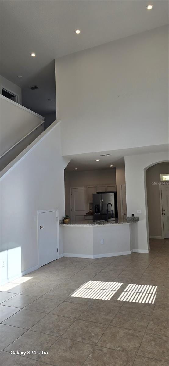 unfurnished living room featuring light tile patterned flooring, a towering ceiling, and sink