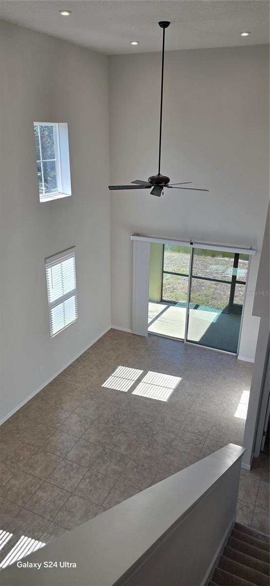 unfurnished living room with tile patterned flooring, a towering ceiling, and ceiling fan