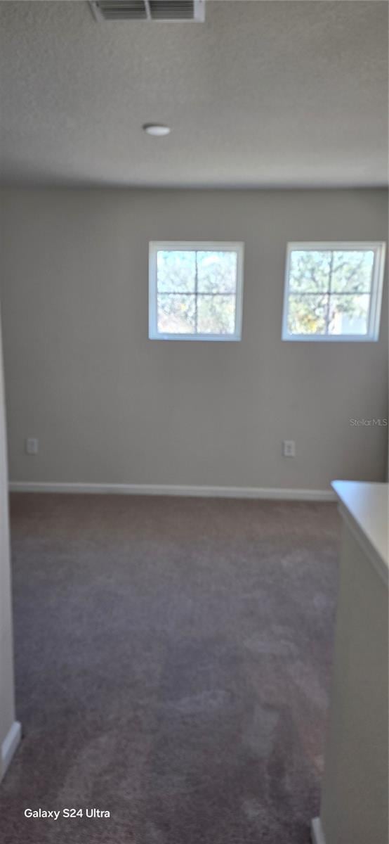 empty room with dark carpet, plenty of natural light, and a textured ceiling