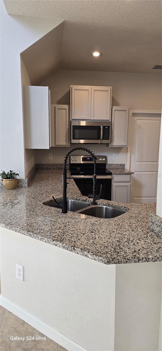 kitchen with appliances with stainless steel finishes, white cabinetry, sink, light stone counters, and a textured ceiling