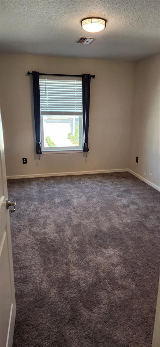 unfurnished room featuring dark colored carpet and a textured ceiling