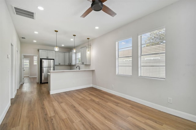 kitchen with hanging light fixtures, light hardwood / wood-style flooring, stainless steel fridge, and kitchen peninsula