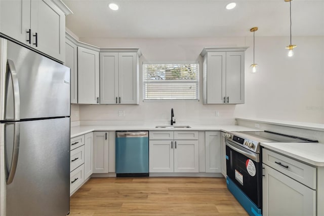 kitchen with appliances with stainless steel finishes, decorative light fixtures, sink, and light wood-type flooring