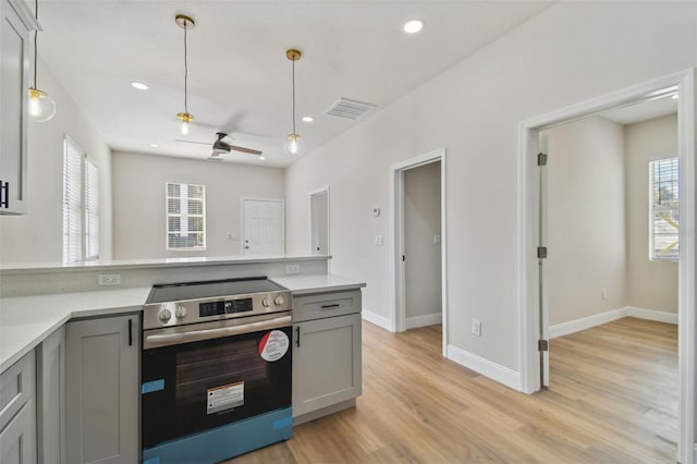 kitchen featuring gray cabinets, stainless steel electric range oven, hanging light fixtures, and light wood-type flooring