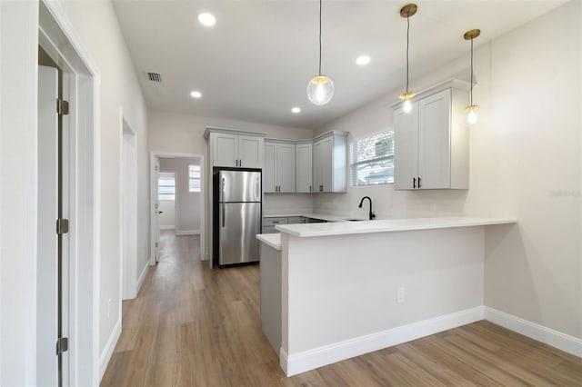 kitchen with hanging light fixtures, sink, stainless steel refrigerator, and kitchen peninsula