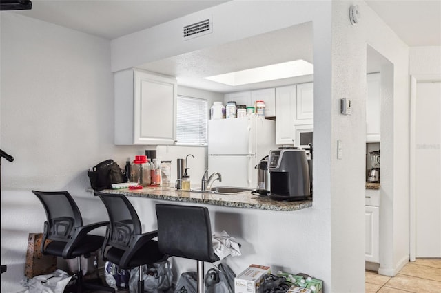 kitchen featuring sink, light tile patterned floors, white refrigerator, kitchen peninsula, and white cabinets