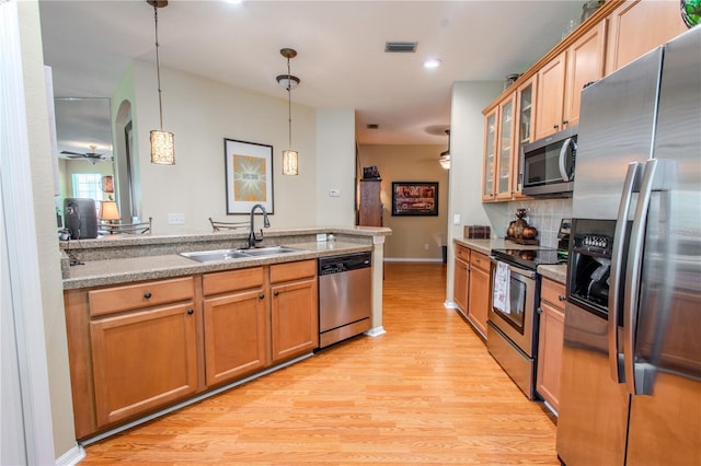 kitchen with pendant lighting, sink, light hardwood / wood-style flooring, stainless steel appliances, and decorative backsplash