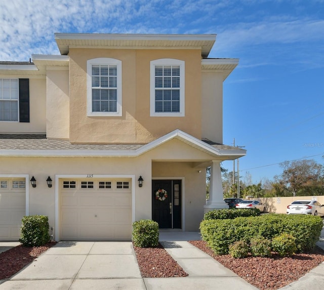 view of property with stucco siding, a garage, driveway, and a shingled roof