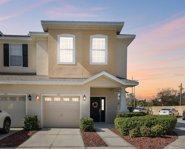 townhome / multi-family property with stucco siding, an attached garage, roof with shingles, and driveway