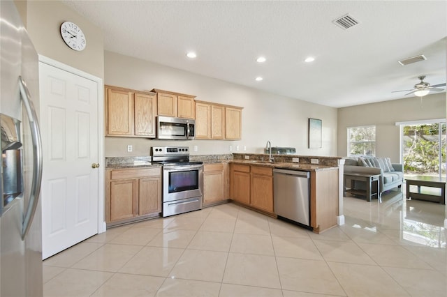 kitchen with sink, light tile patterned floors, appliances with stainless steel finishes, kitchen peninsula, and dark stone counters