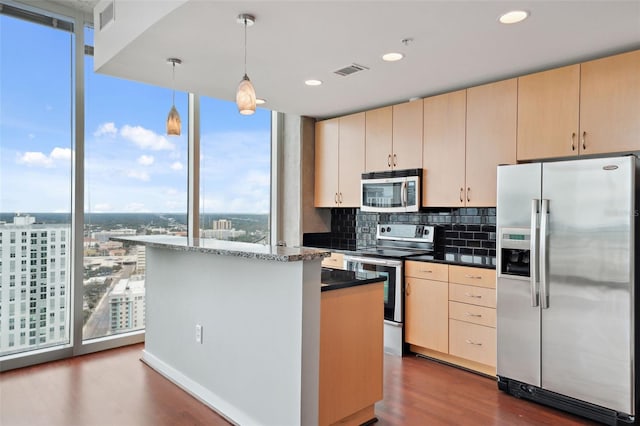 kitchen featuring stainless steel appliances, light brown cabinetry, hanging light fixtures, and backsplash