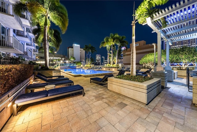 patio at twilight with a community pool and a pergola