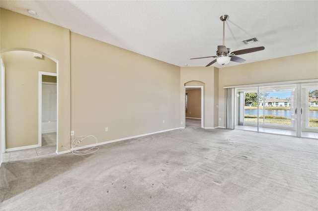 unfurnished living room with a water view, ceiling fan, light carpet, and a textured ceiling