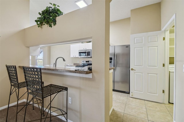 kitchen featuring white cabinets, a kitchen breakfast bar, light tile patterned floors, kitchen peninsula, and stainless steel appliances