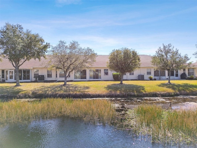 rear view of property featuring a water view, cooling unit, and a lawn