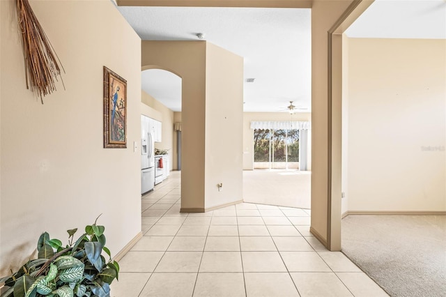 corridor featuring arched walkways, light carpet, baseboards, and light tile patterned floors