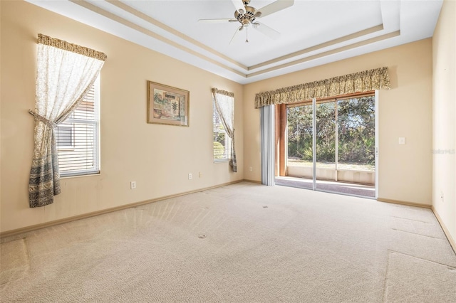 unfurnished room featuring a tray ceiling, carpet, plenty of natural light, and baseboards