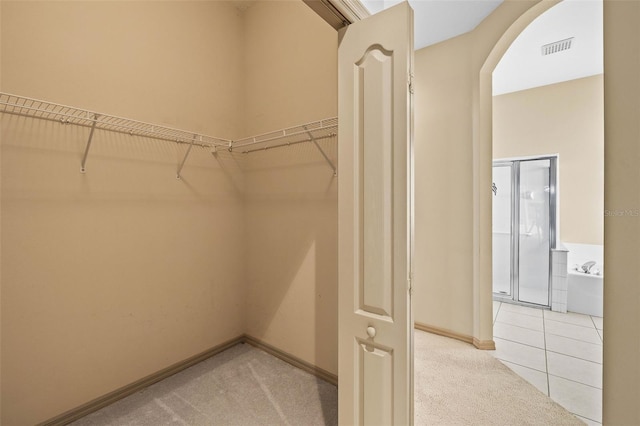 spacious closet featuring visible vents, arched walkways, carpet flooring, and tile patterned floors