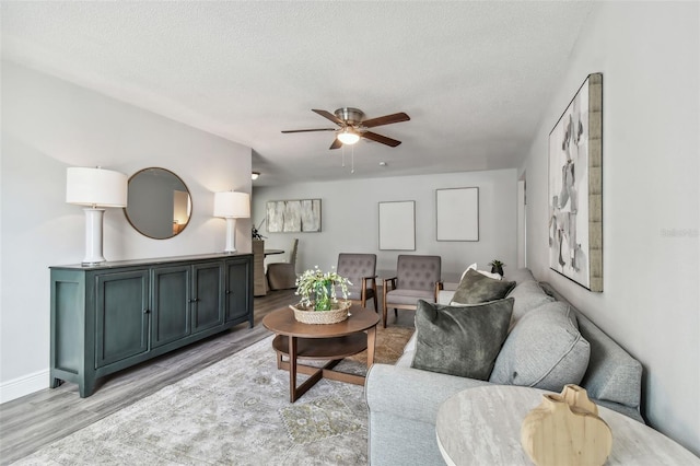 living room with ceiling fan, a textured ceiling, and light wood-type flooring