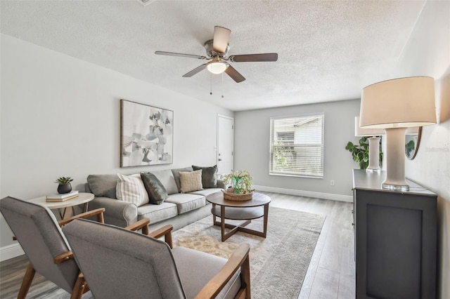 living room with a textured ceiling, ceiling fan, and light hardwood / wood-style flooring