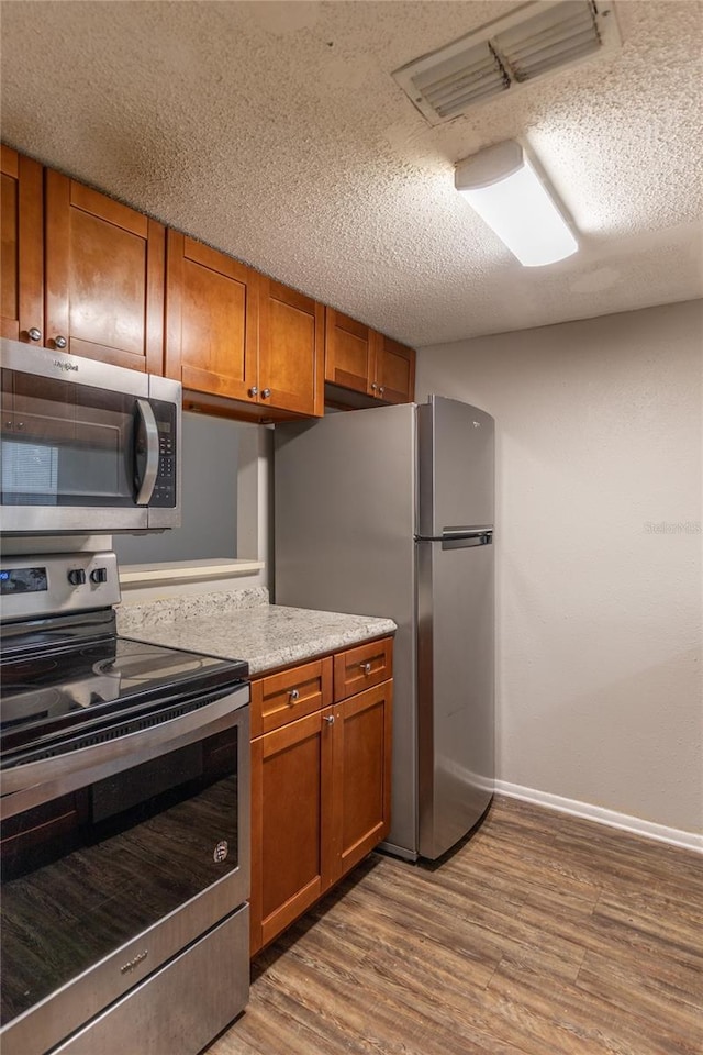 kitchen with light wood-type flooring, a textured ceiling, and appliances with stainless steel finishes