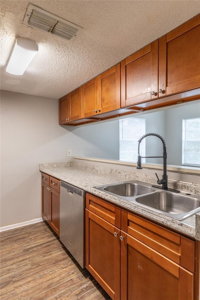 kitchen with stainless steel dishwasher, sink, a textured ceiling, and light wood-type flooring